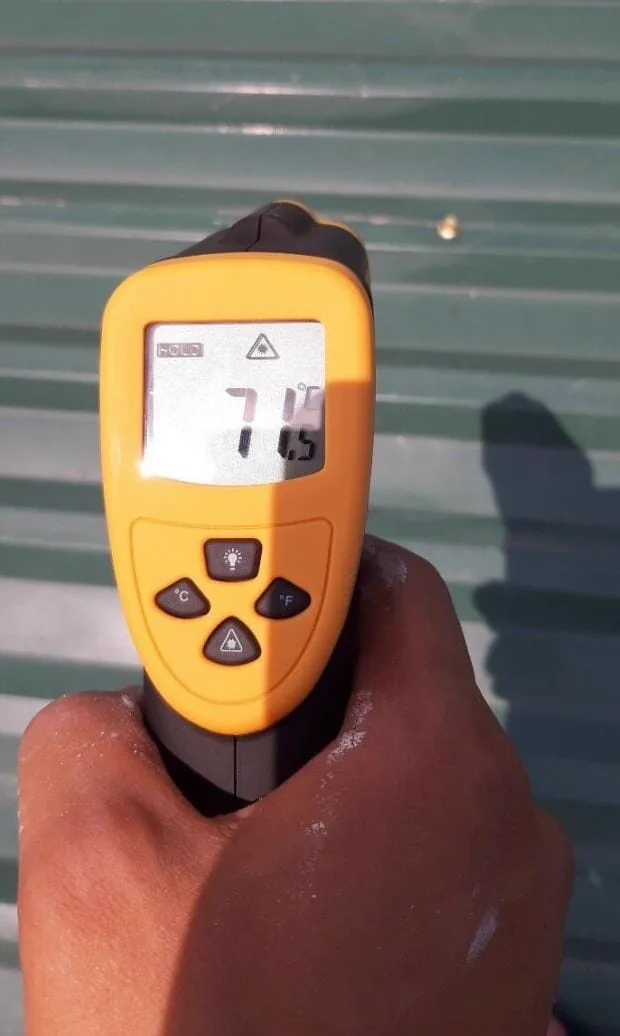 Infrared thermometer reading 71.5&deg;C on an uncoated green metal roof